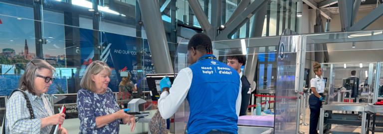 Un facilitateur de l'ACSTA aide une passagère à passer au contrôle de sûreté à l'aéroport.