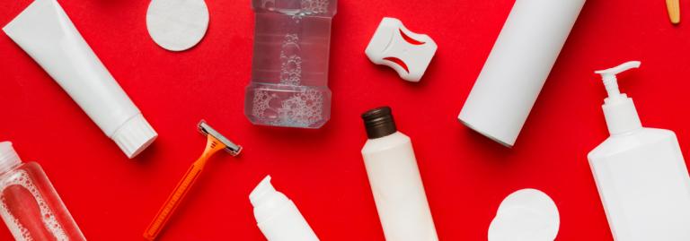 Une variété de produits de soins personnels, y compris un rasoir, une brosse à dents et divers contenants, sont posés sur une surface rouge.