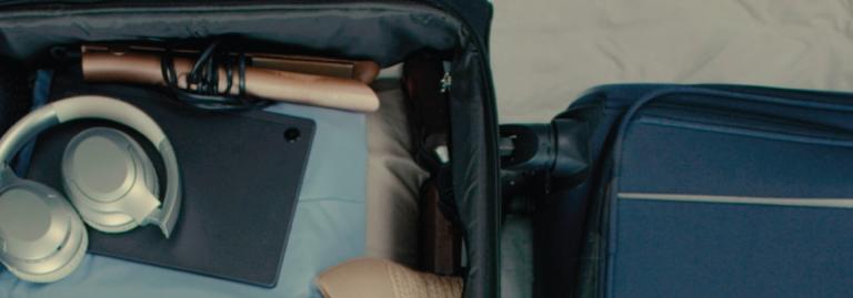 Valise ouverte avec un ordinateur portable, des écouteurs et un fer à lisser.