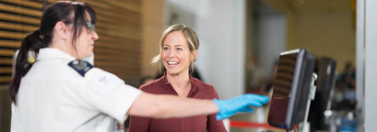 A female screening officer points to a monitor while a passenger smiles at her.