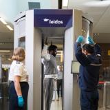 A screening officer is showing a passenger how to stand with their arms up in a full body scanner. 
